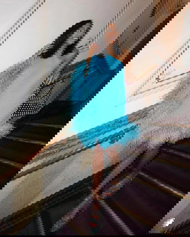 Девушка в коротком голубом платье с перьями спускается по лестнице; игривый и лёгкий праздничный образ с блеском в обуви.