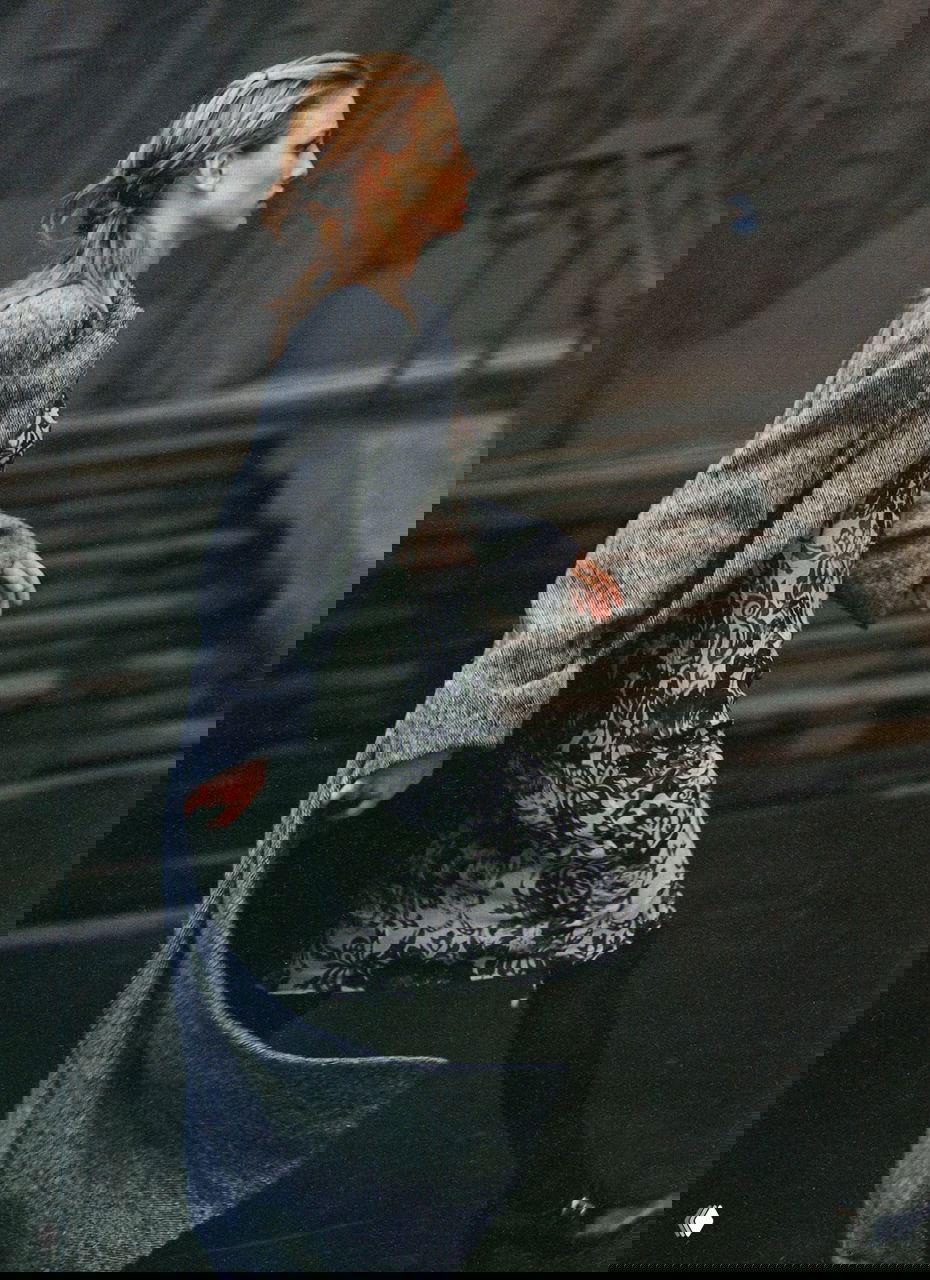 Динамичный кадр: модель в длинном пальто с развевающимся подолом идёт по ступеням городского пейзажа, расфокусированный фон и естественный свет.