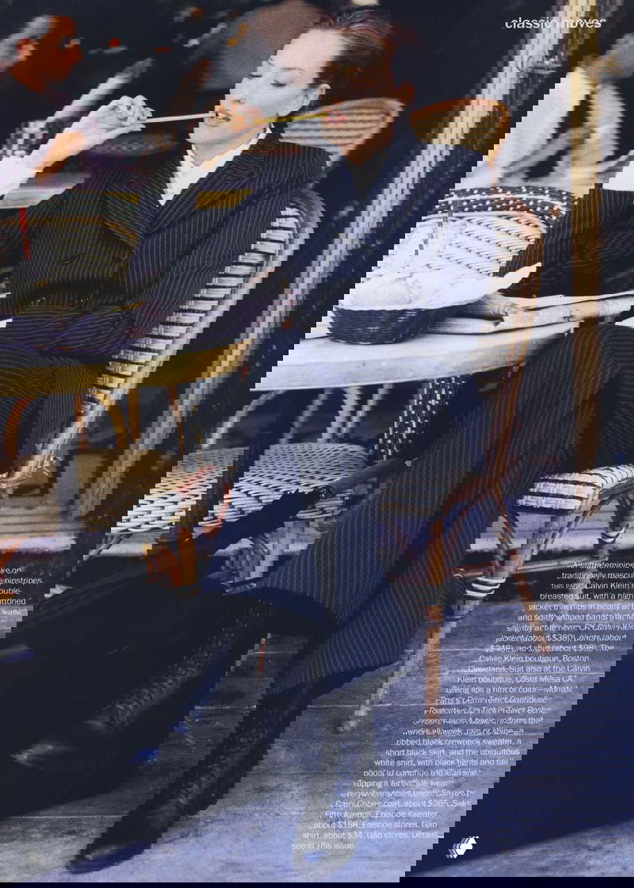 Сидящая модель в пинстрайп-костюме в уличном кафе; композиция подчёркивает классическую офисную эстетику 90-х.