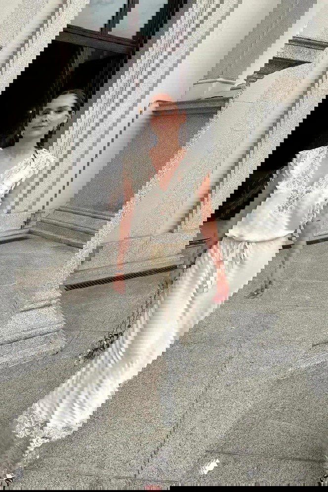 Женщина в кремовом длинном платье с кружевными деталями идёт по парадной зоне; спокойный пастельный образ с нейтральным макияжем.