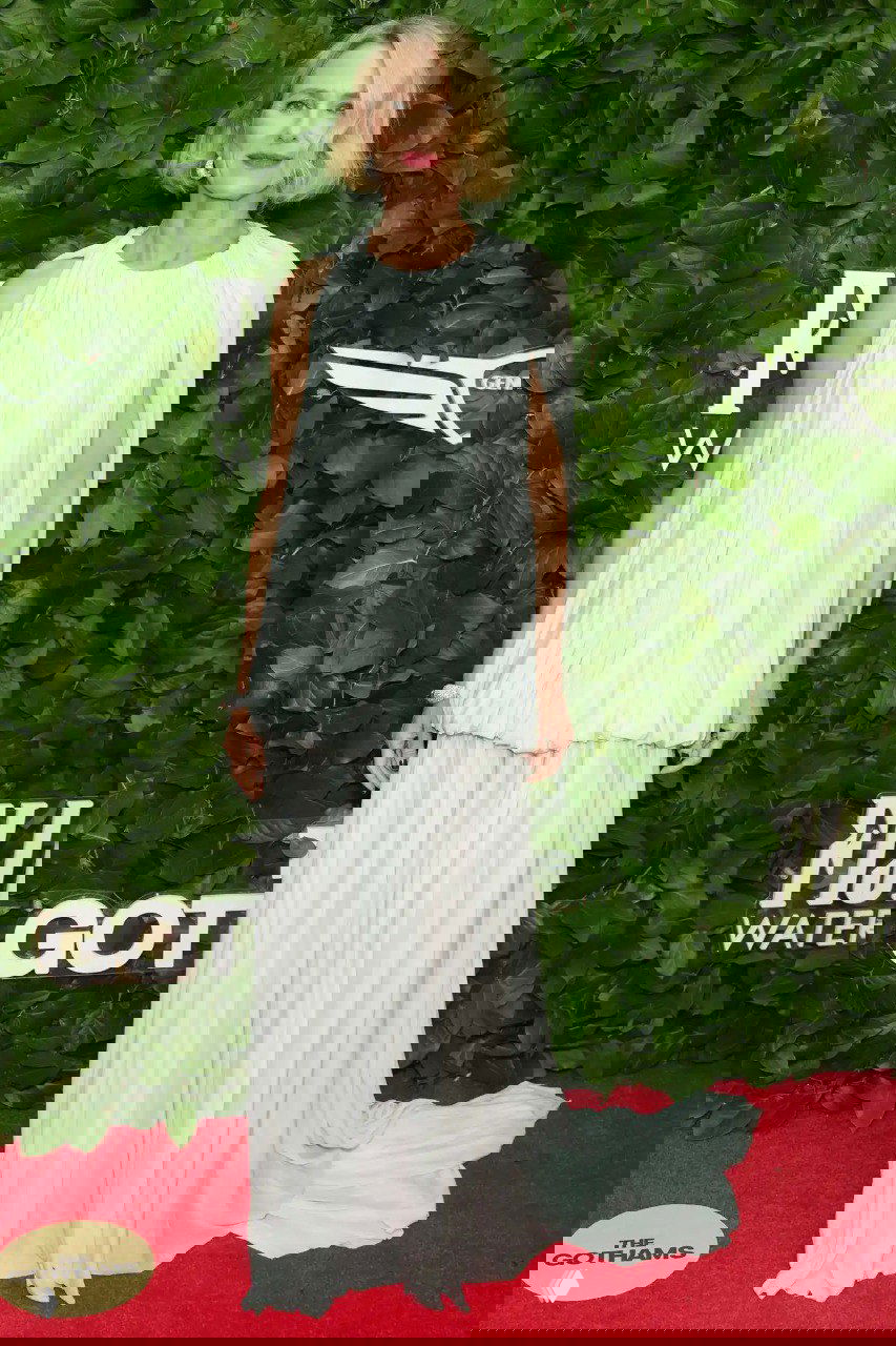 Наоми Уоттс в светлом многослойном платье на красной дорожке Gotham TV Awards 2025: нежный пастельный образ на фоне зелёной фотостены.