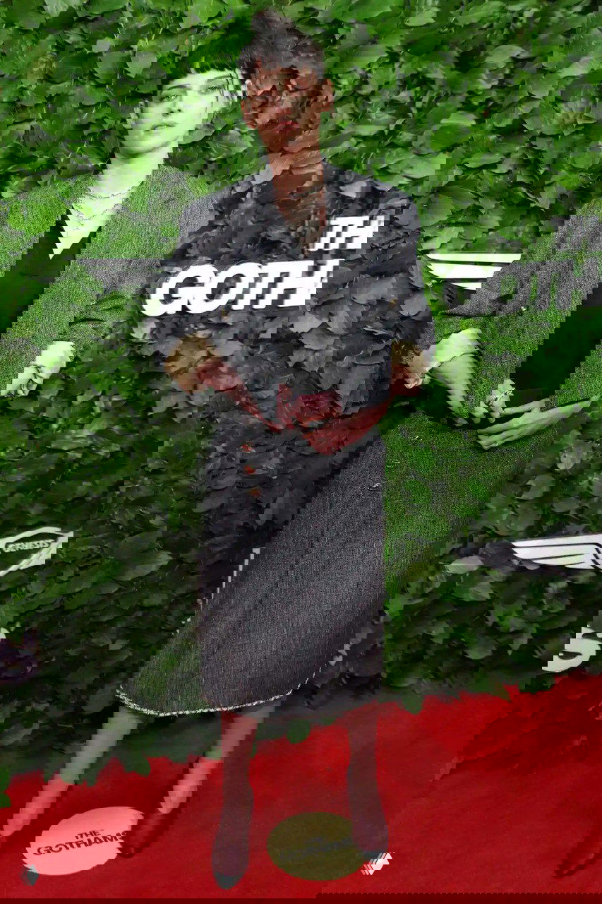 Кристен Стюарт в строгом костюме и юбке миди на красной дорожке Gotham TV Awards 2025: рубленый силуэт и стильный образ на фоне зелёной стены.