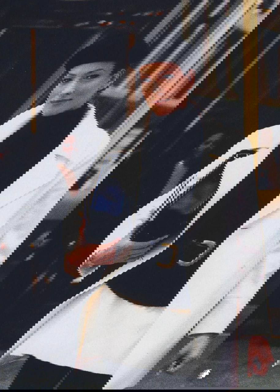 Модель в белом пальто и берете на входе в здание; элегантный офисный образ, подчёркнутый аксессуарами в стиле 90-х.