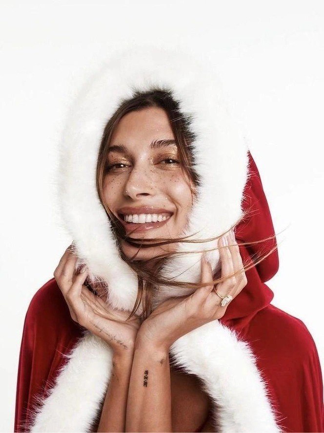 Улыбающаяся женщина в красном капюшоне с белой меховой отделкой — крупный план лица с лёгким натуральным макияжем и праздничным настроением.