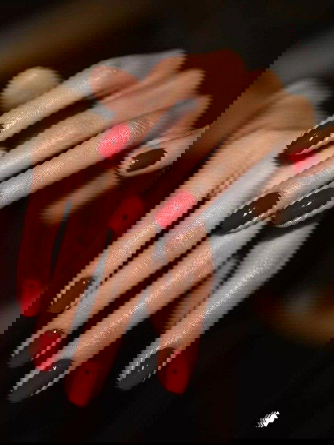 Руки с ярким глянцевым красным маникюром на овальных ногтях, крупный план пересечённых пальцев на тёмном фоне — праздничный акцент.