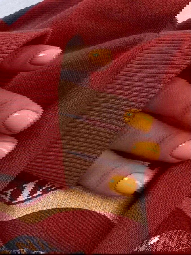 Короткие ногти ярко-жёлто-оранжевого оттенка, пальцы на фоне тёплого красного свитера — контрастный и уютный праздничный вариант.