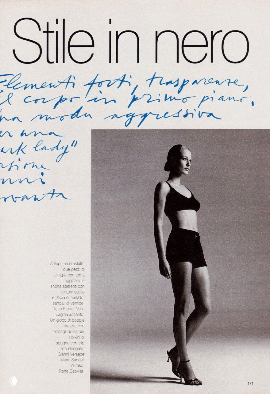 Чёрно‑белый студийный кадр: женщина в минималистичном образе в коротком топе и шортах, строгая модельная поза и высокие каблуки, fashion‑стиль.