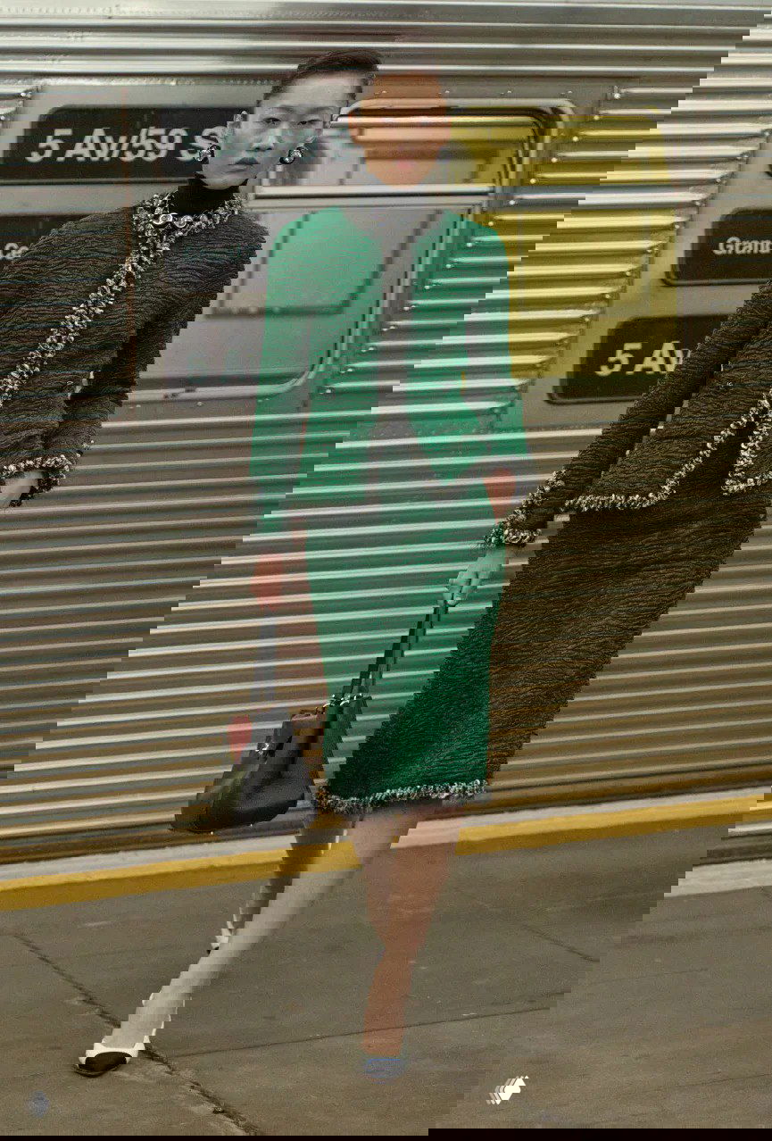 Модель в зелёном твидовом костюме Chanel идёт по платформе нью‑йоркского метро во время показа Матье Блази, на фоне вагона и навигации.