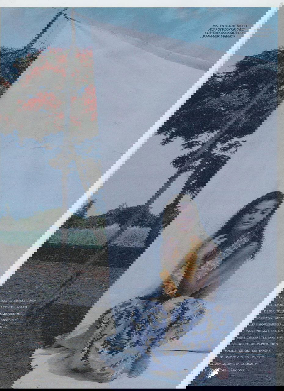 Модель сидит перед белым полотнищем на фоне тропического пейзажа; приглушённые тона и атмосфера ретро-фотосъёмки 1992 года.