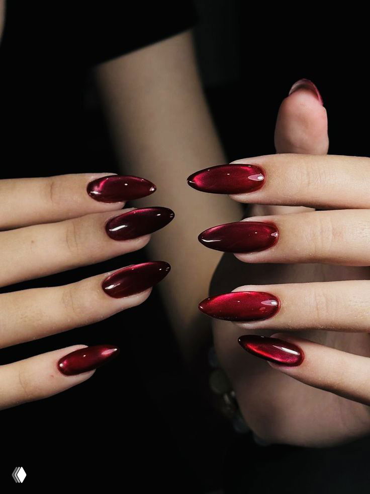 Руки с удлинёнными красными глянцевыми ногтями «балерина» в глубокем бордовом оттенке на тёмном фоне с бликами света.