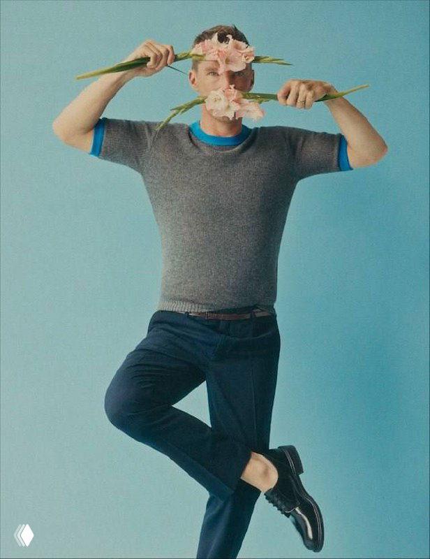 Портрет Бенедикта Камбербэтча в студии на голубом фоне: актёр держит крупные розовые цветы, стильная глянцевая эстетика съёмки.