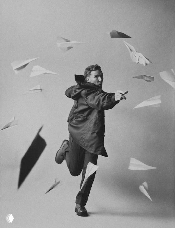 Чёрно‑белая фотография Бенедикта Камбербэтча в движении среди бумажных самолётиков: динамичная художественная постановка.