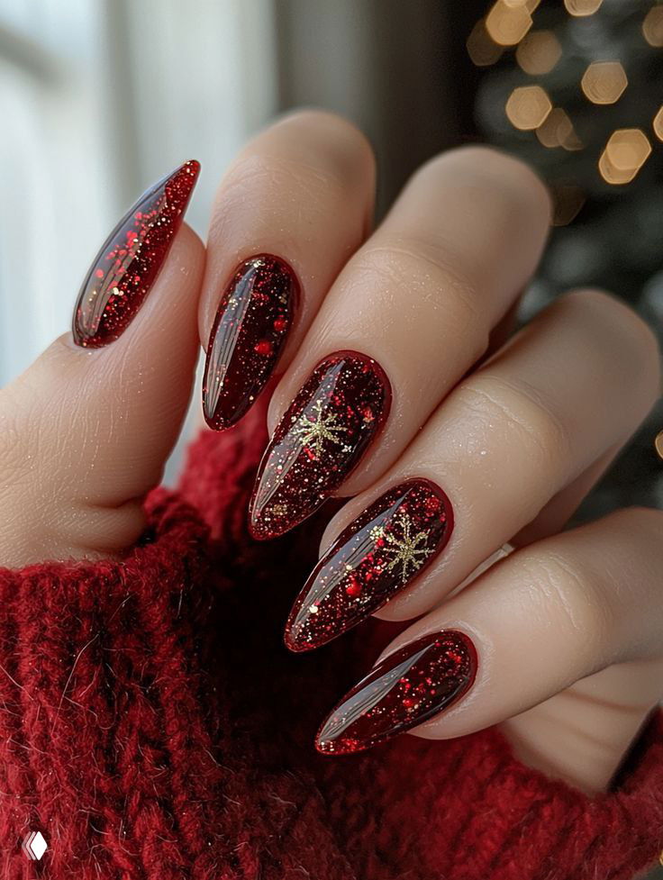Маникюр с длинными острыми ногтями, тёмно‑красный лак с красными блёстками и золотыми декоративными элементами, виден перстень на пальце.
