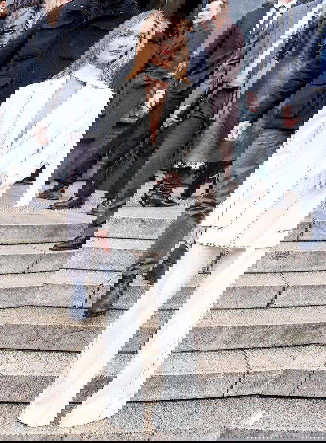 Роузи в белом брючном костюме с длинными расклёшенными штанами и шарфом‑деталью — пример классики с лёгкой оригинальностью