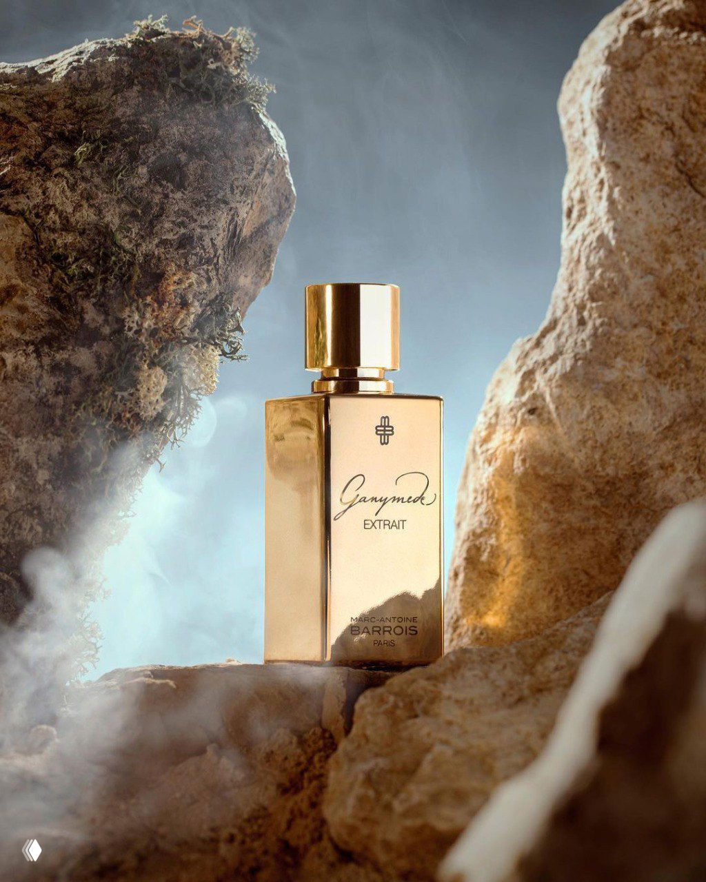 Золотой флакон Marc‑Antoine Barrois Ganymede Extrait в окружении камней и лёгкого тумана — атмосферный рекламный кадр аромата.
