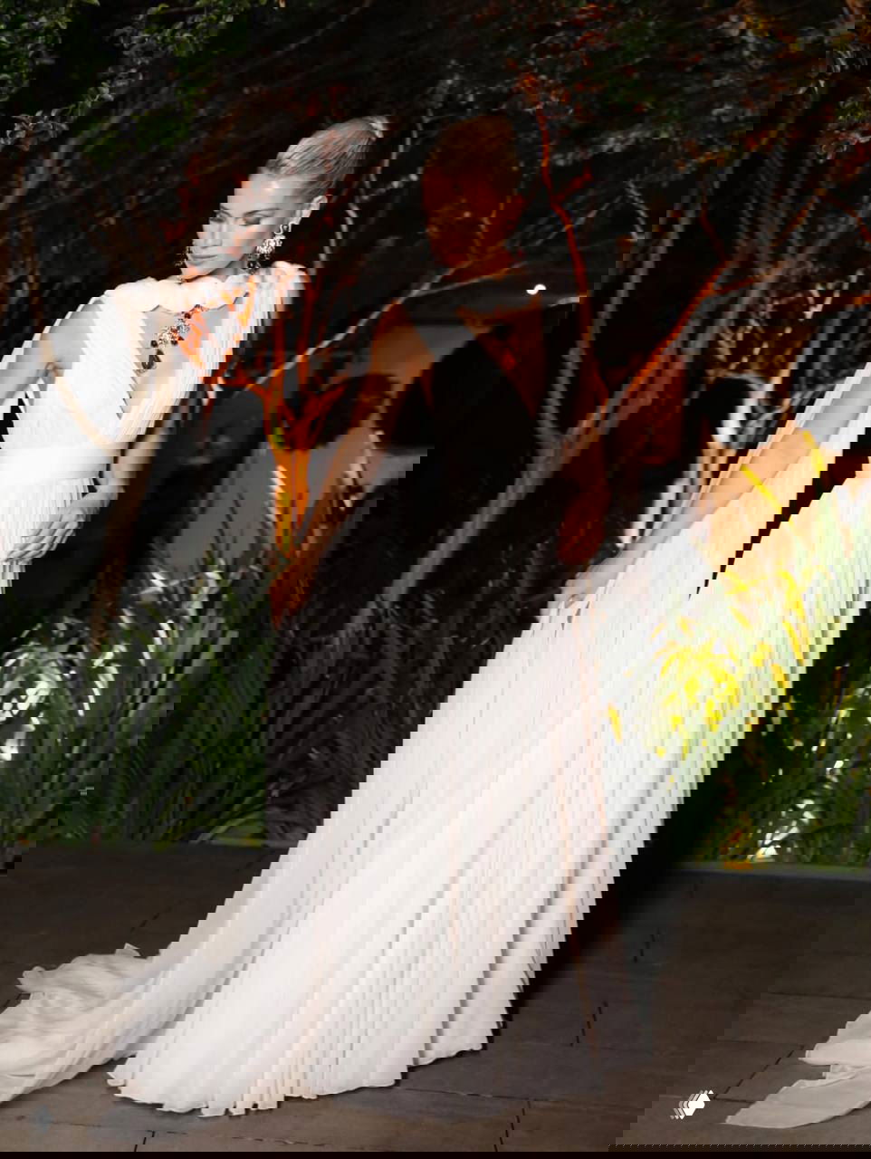 Китти Спенсер в длинном белом платье с воздушным шлейфом и крупным золотым колье с рубиновыми подвесками на вечернем мероприятии на открытом воздухе.