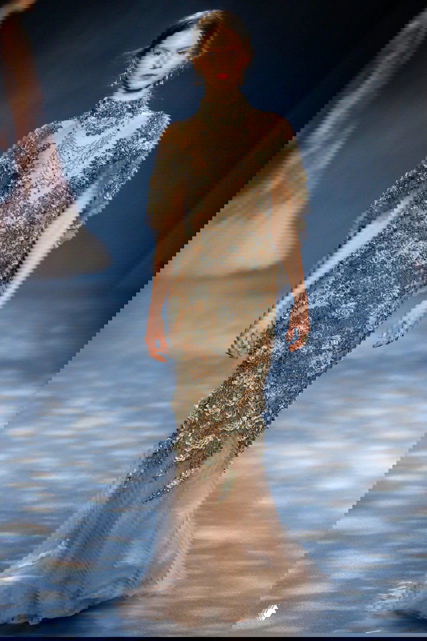 Изящное платье Marchesa с богатой бисерной и вышивальной отделкой в золотисто‑бежевой гамме, украшенное массивными украшениями у шеи.