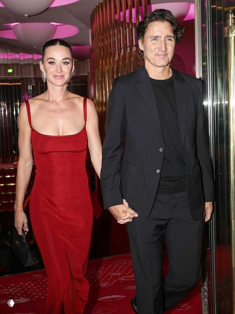 Женщина в обтягивающем красном платье и мужчина в тёмном костюме идут по красной дорожке клуба, держась за руки.