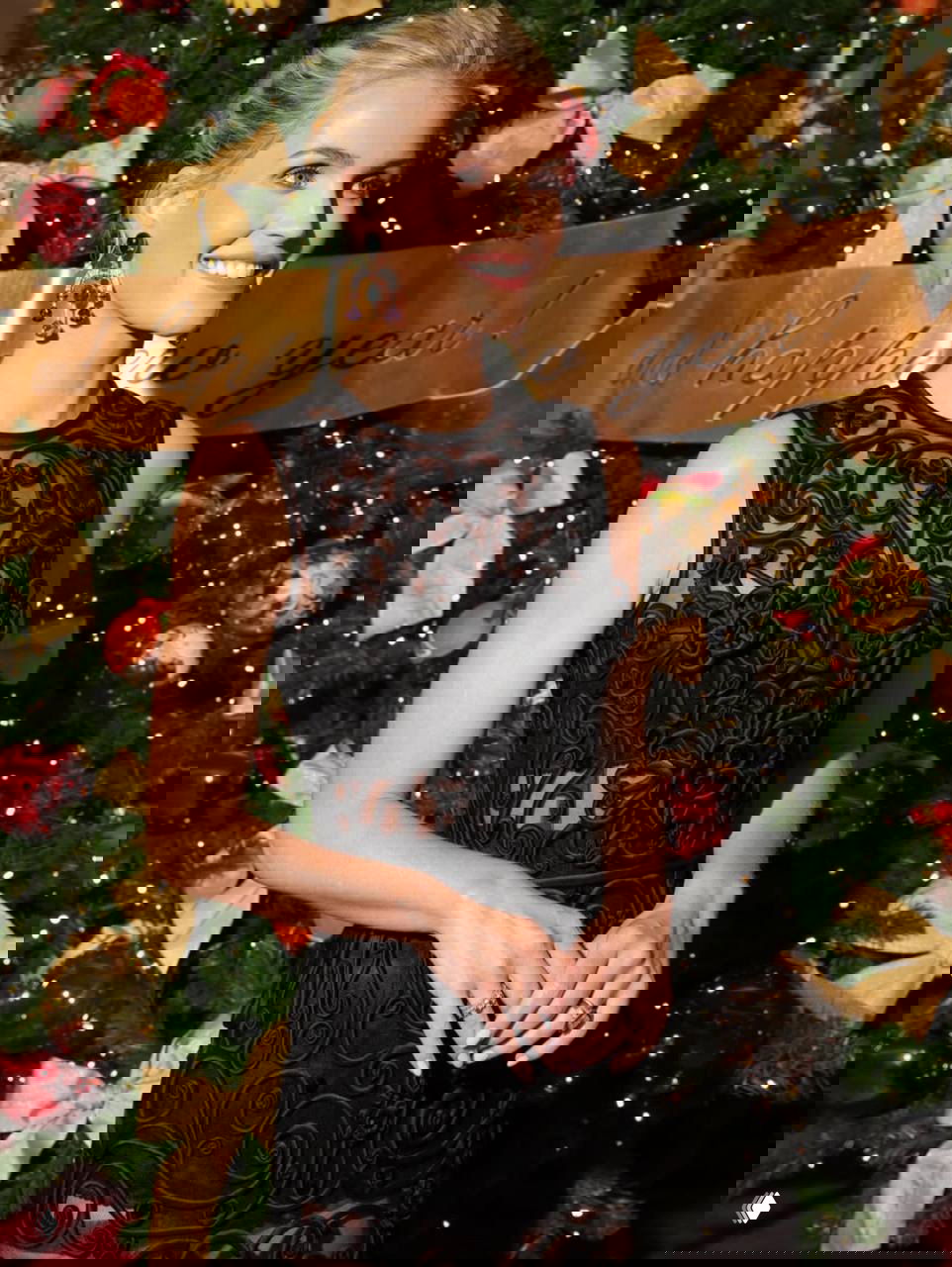 Китти Спенсер улыбается на фоне рождественской ёлки в чёрном платье и крупными разноцветными серьгами, праздничная атмосфера и украшения сцены.