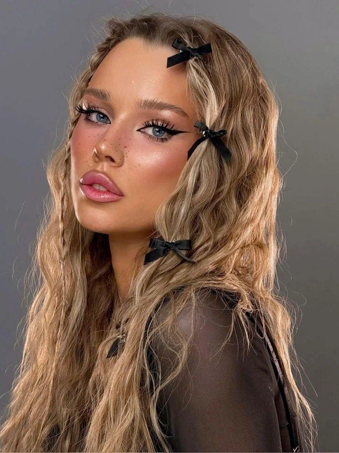 Портрет модели с выразительными стрелками, длинными ресницами и ухоженными губами; праздничный макияж и декоративные бантики в волосах.