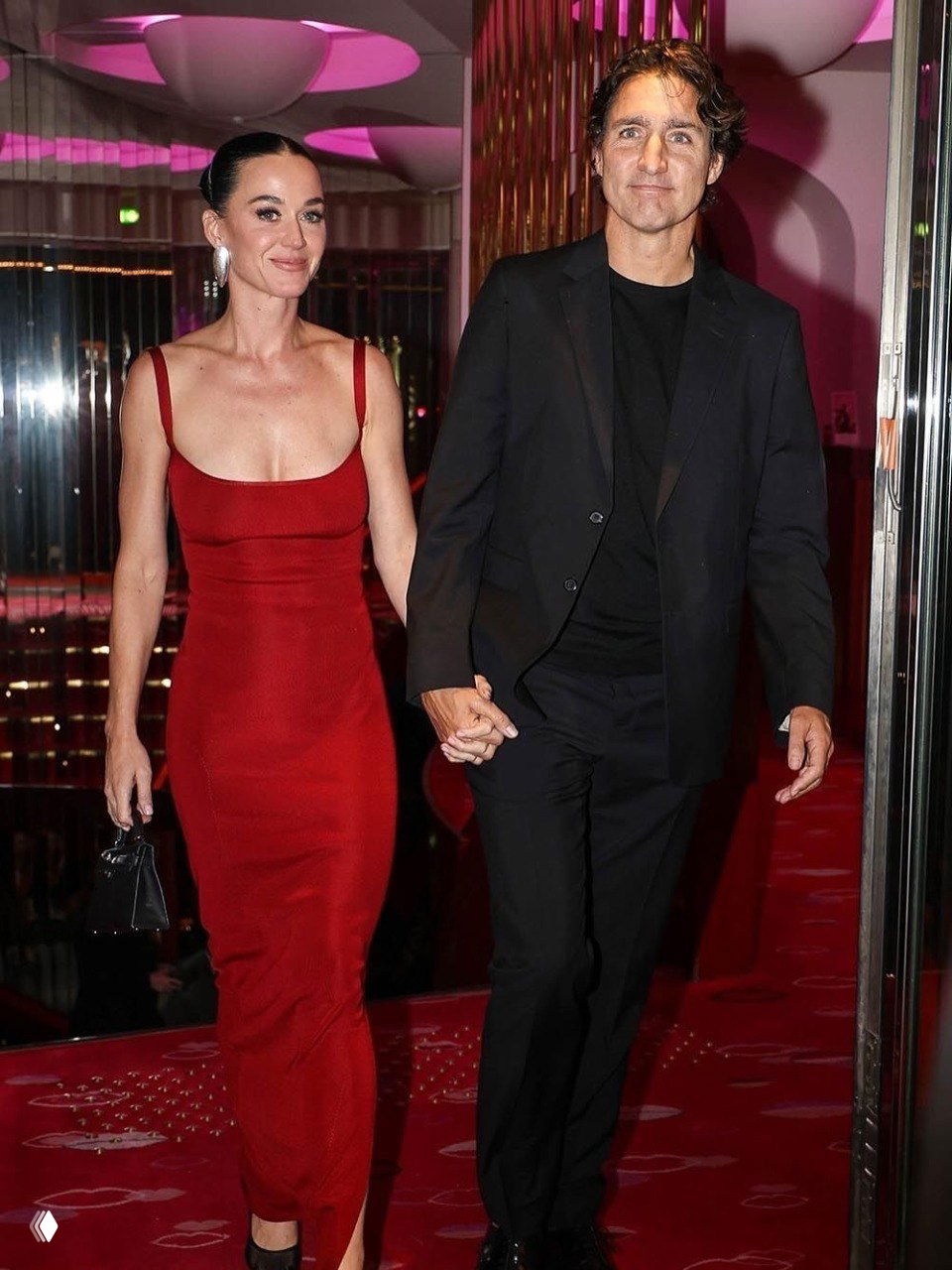 Пара в вечерней одежде идёт по коридору клуба с розовой подсветкой: красное платье и тёмный костюм, рука об руку.