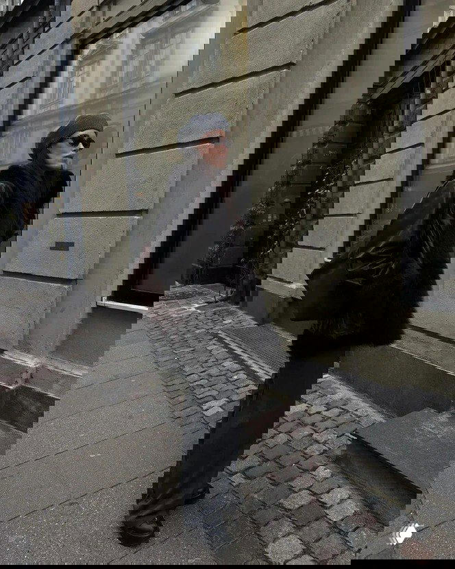 Женщина в сером берете и тёмной верхней одежде идёт по городской улице в минималистичном образе — пример французской элегантности и уличной моды.