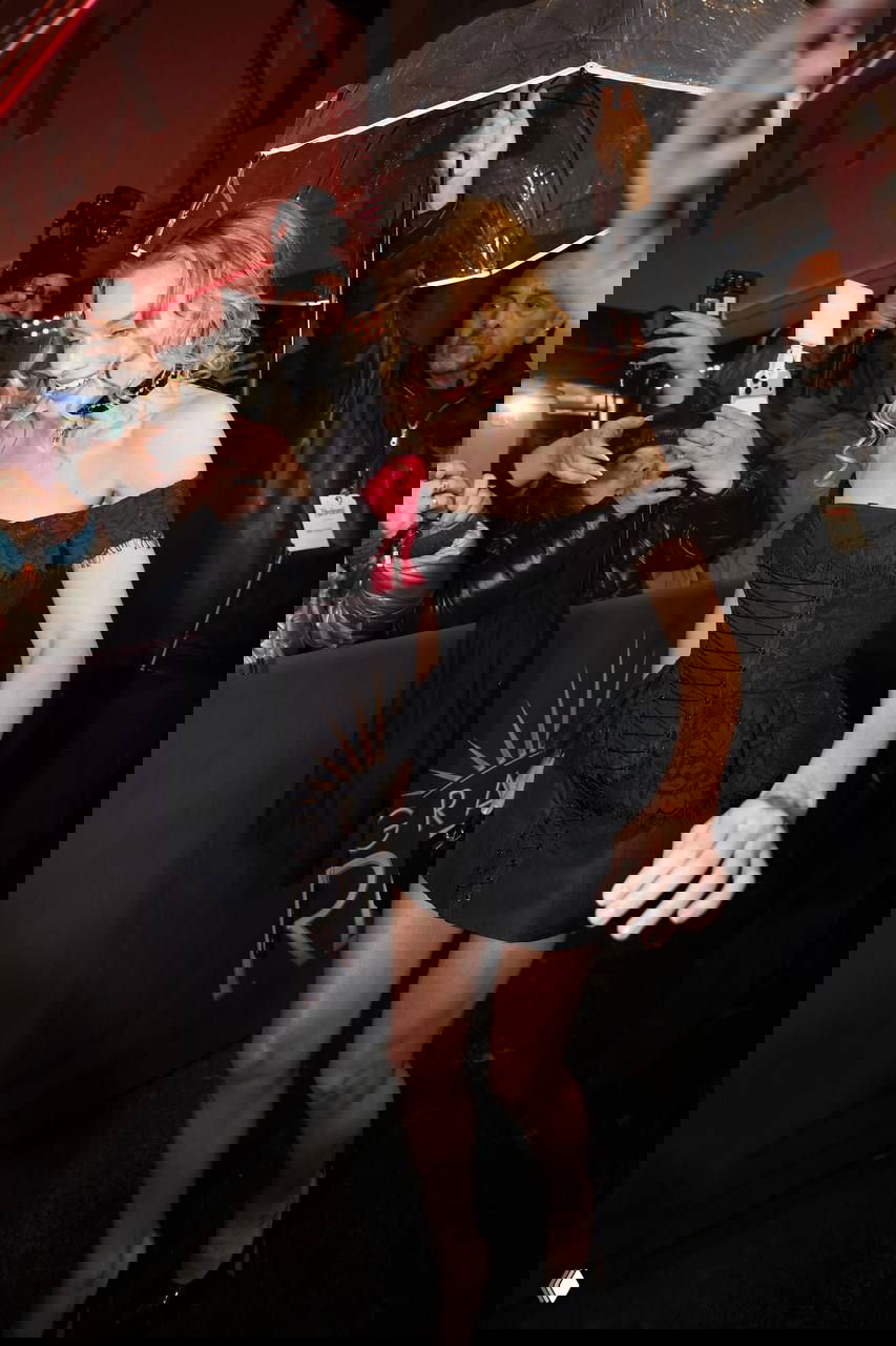 Марго Робби пробирается сквозь толпу фотографов и поклонников под прозрачным зонтом, чёрное мини‑платье и каблуки в кадре на афтерпати.