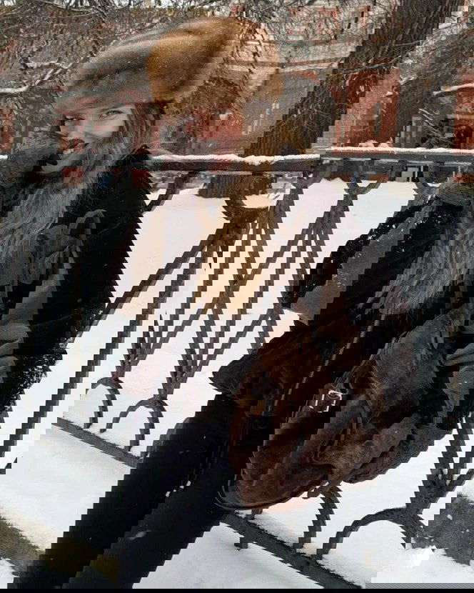 Модель в большой меховой шапке и тёплой куртке на фоне заснеженного парка — образ в славянском стиле с акцентом на тепло и текстуру меха.