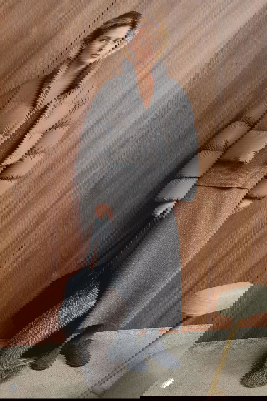 Женщина в укороченном сером пуховике и трикотажном комплекте, большая сумка с меховым аксессуаром на фоне деревянной стены — фотосессия Marie Claire, подчёркнута уютная городская эстетика.