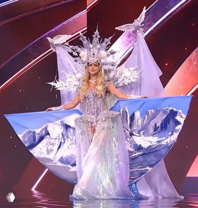 Лёгкий серебристо‑голубой костюм в ледяной тематике с большой круговой декорацией позади и водной стилистикой на фоне сценического оформления.