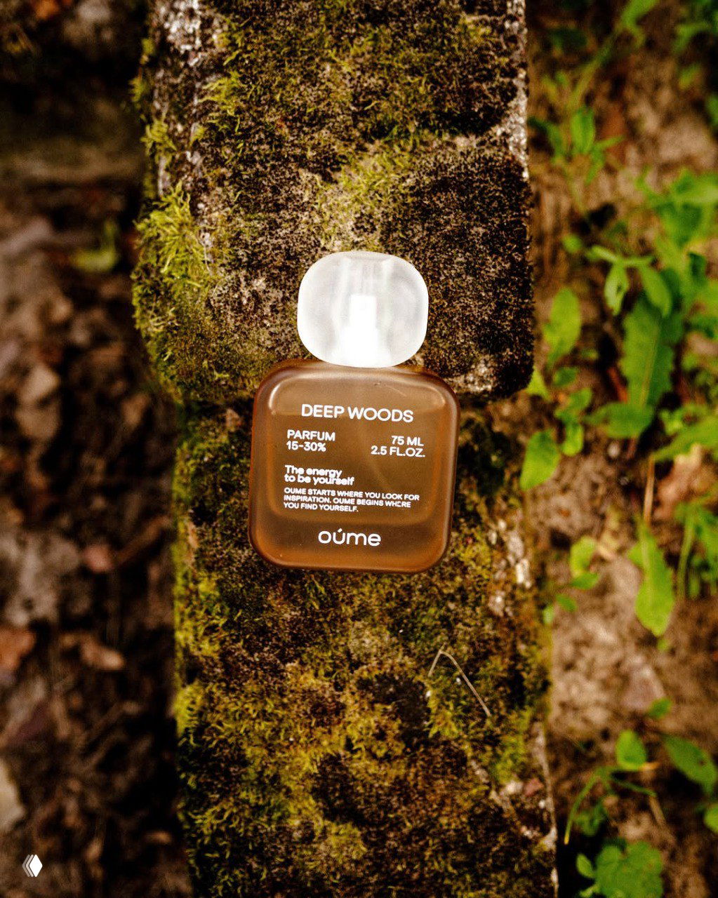 Флакон Oumé Deep Woods, установленный на покрытой мхом поверхности дерева; тёплые древесные тона подчёркивают идею «нагреть лес» и природные аккорды парфюма.