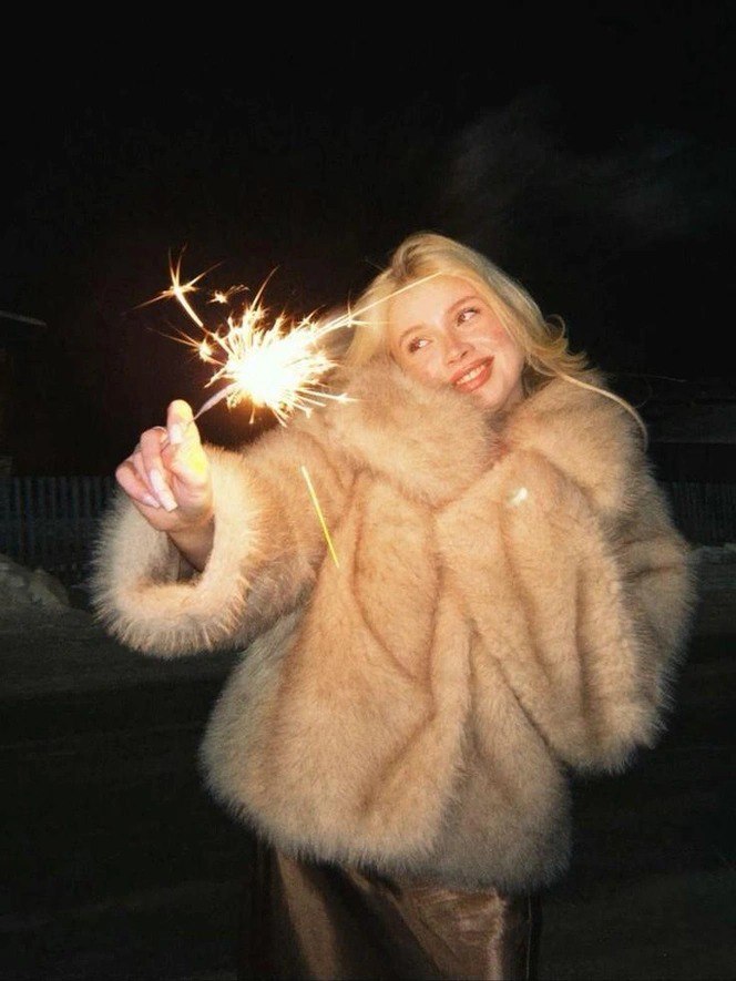 Девушка в пушистой шубе держит бенгальский огонь ночью — праздничный зимний кадр, иллюстрация постпраздничной атмосферы и ухода за кожей.