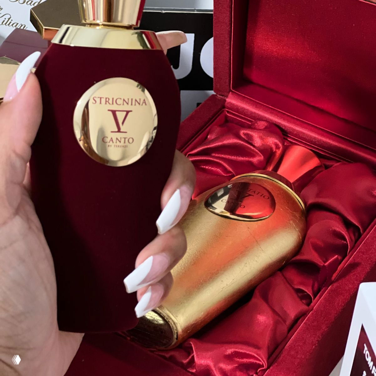 Флакон V Canto Stricnina в руках на фоне бархатной коробки: красный корпус флакона и золотые детали создают ощущение контраста и роскоши.