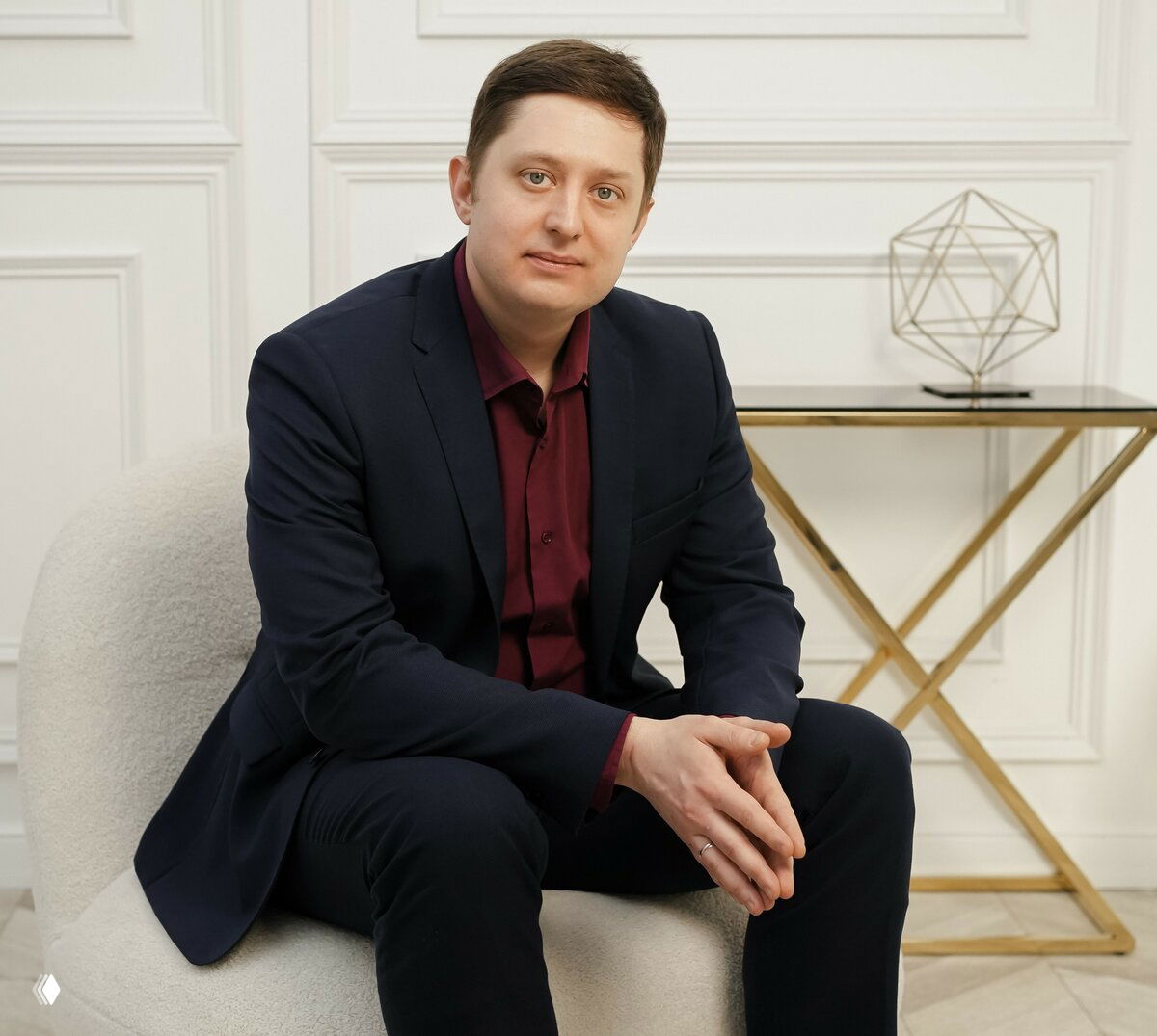 Портрет мужчины в костюме, сидящего в кресле на светлом фоне с столиком — фото для анонса психологической практики.