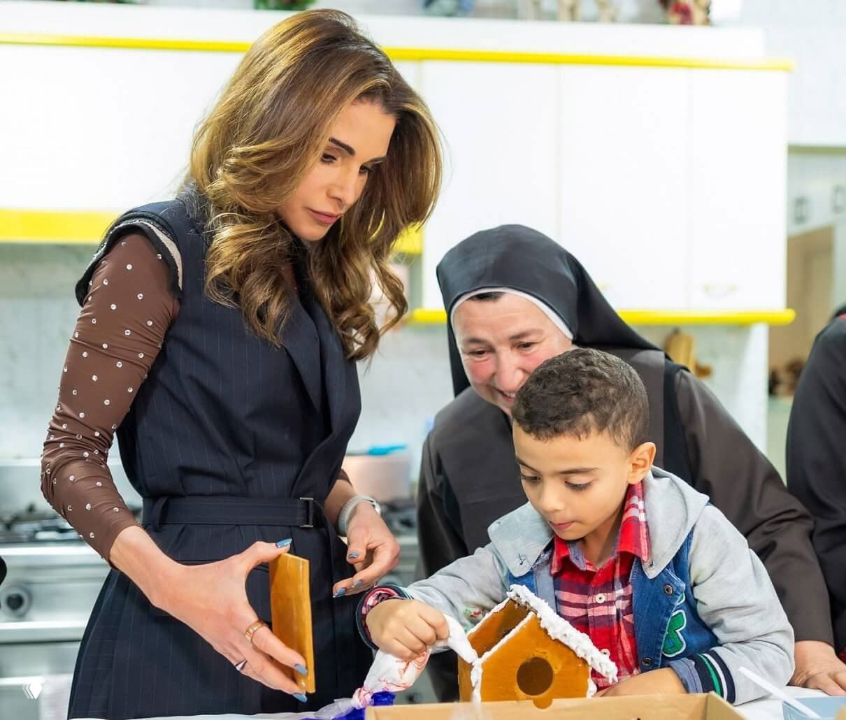 Рания помогает мальчику собирать пряничный домик на рождественском мастер-классе в благотворительном обществе «Мар Мансур».