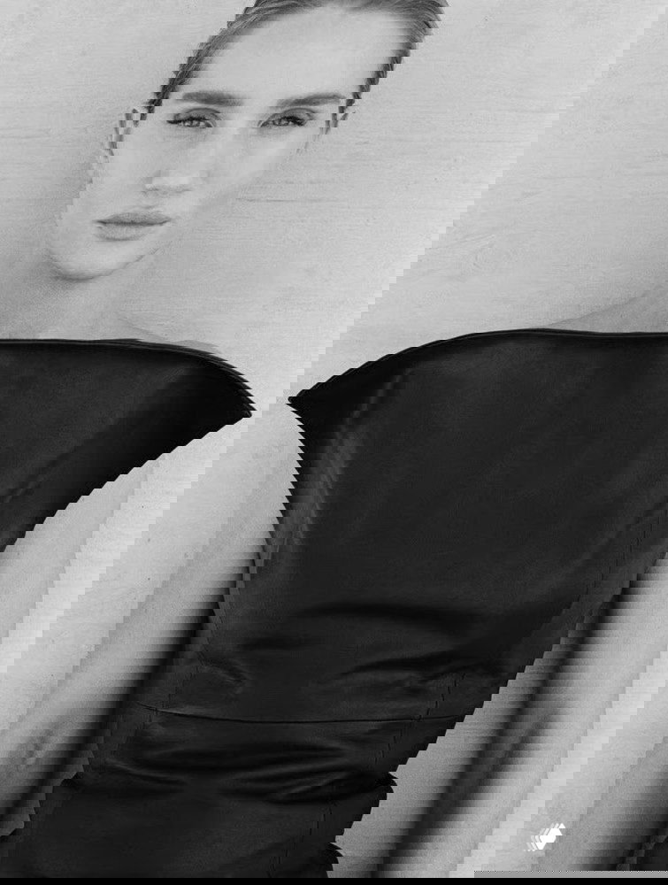 Чёрно‑белый студийный портрет женщины‑модели в строгом тёмном верху, крупный план лица и плеч, минималистичная рекламная фэшн‑фотография.