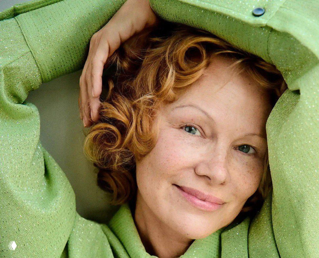 Крупный план портрета улыбающейся женщины в зелёном свитере, естественный макияж и мягкий свет интерьерной съёмки, ненавязчивая атмосфера.