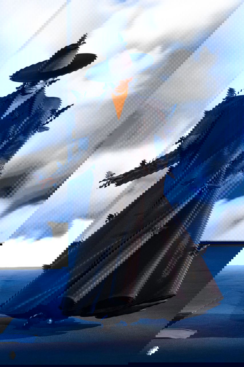 Чёрное структурированное пальто-манто от Роберта Вуна с объёмными плечами и декоративными элементами в виде лепестков, модель шагает по подиуму.