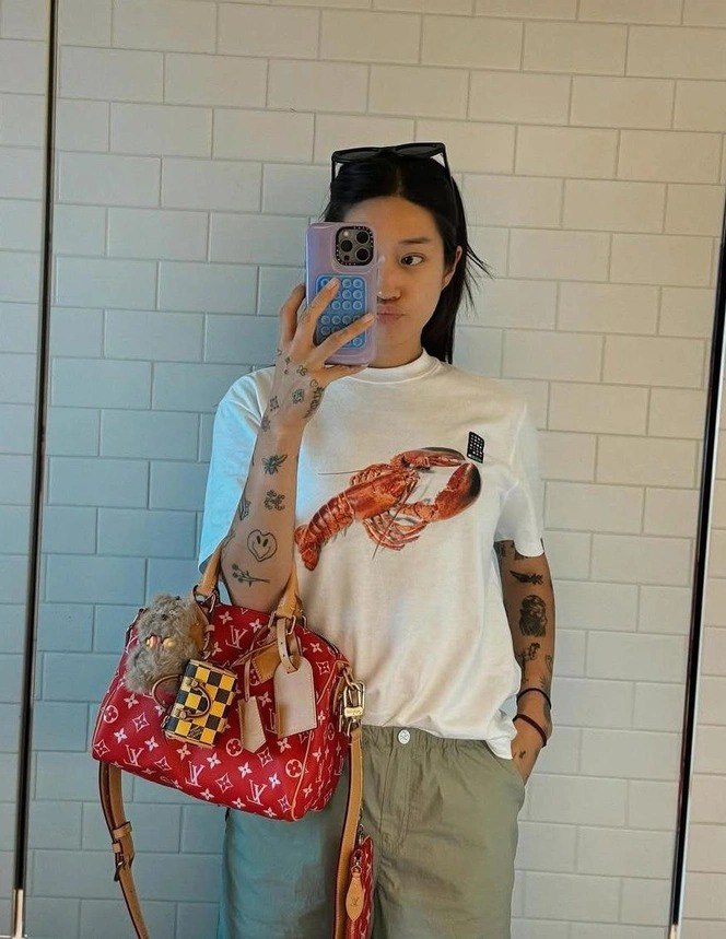 Селфи в зеркале: человек в белой футболке с принтом омара держит крупную красную сумку Louis Vuitton с брелоком на ручке.