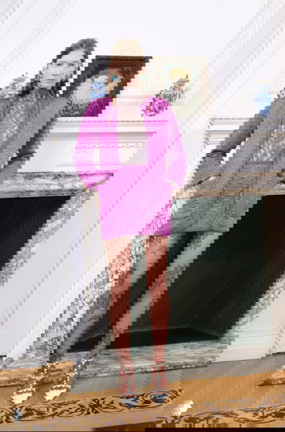 Яркий фиолетовый жакет и кружевные колготки на модели у мраморного камина — насыщенный цветовой акцент в Pre‑Fall 2026 Valentino.