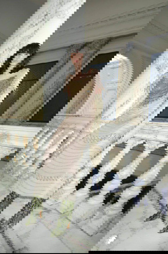 Модель в нежно‑песочном платье с блестящим декором и зелёными сапогами на мраморной лестнице — сочетание текстур и материалов у Valentino.