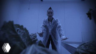 Ольга Бузова в защитном плаще среди растений в учебной агролаборатории — кадр из 3‑го сезона о работе с растениями и животными.