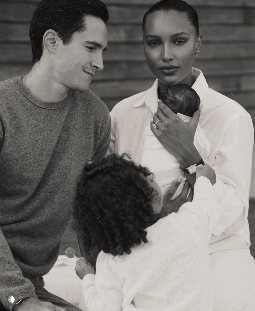 Жасмин Тукс держит новорождённого сына на руках в чёрно‑белой семейной фотографии: рядом муж и старший ребёнок, тёплая сцена после родов.