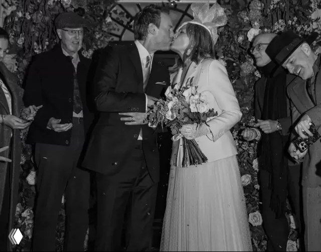 Черно‑белый кадр: молодожёны целуются среди гостей, вокруг конфетти и радостные лица — динамичный момент закрытой церемонии.