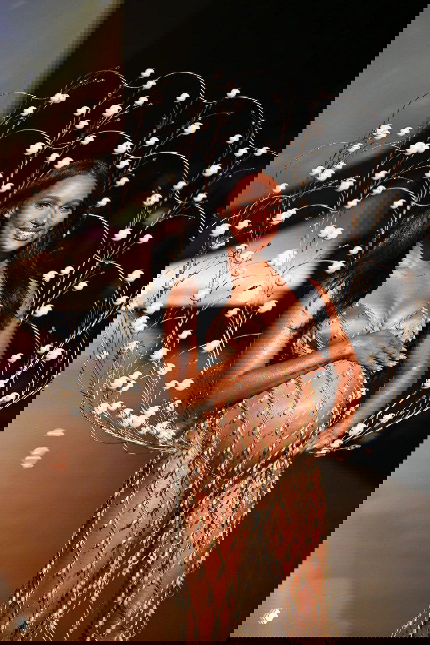 Ещё один кадр Жасмин Тукс на подиуме Victoria’s Secret в наряде с орнаментом, улыбается и держит руку на животе — момент с показа перед родами.