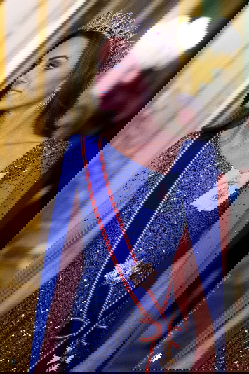 Женщина в синем сверкающем платье с накидкой и тиарой, лента ордена через плечо, на официальном банкете в Виндзорском замке.