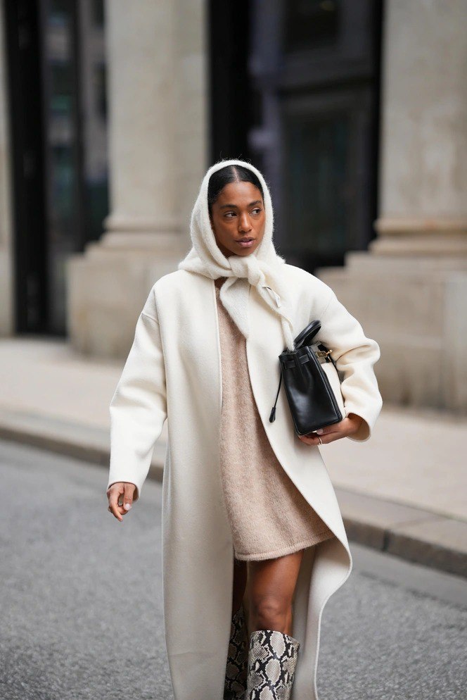 Женщина в светлом пальто и белой шарфокосынке, образ в движении по городской улице, сочетание пальто и тёплой косынки создаёт элегантный зимний лук.