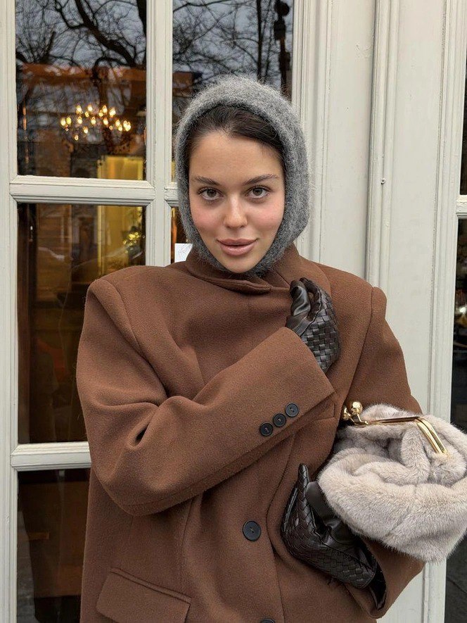 Портрет молодой женщины в коричневом пальто и пушистой шерстяной косынке, сцена у кафе с отражением витрины на заднем плане, зимний аксессуар в фокусе.