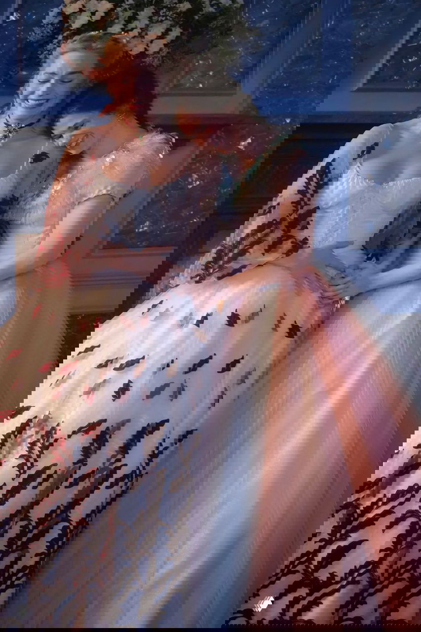 Две актрисы в пышных разноцветных платьях смеются на съемочной площадке; видны вышивка и многослойные юбки в торжественной обстановке.