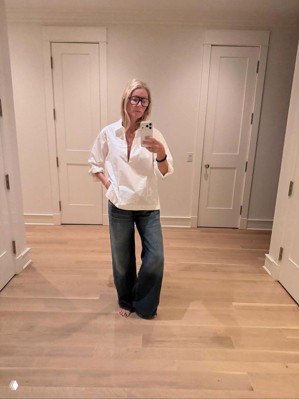 Актриса в свободной белой рубашке и широких джинсах делает селфи в зеркале в просторной светлой комнате, расслабленный городской стиль Gwyn